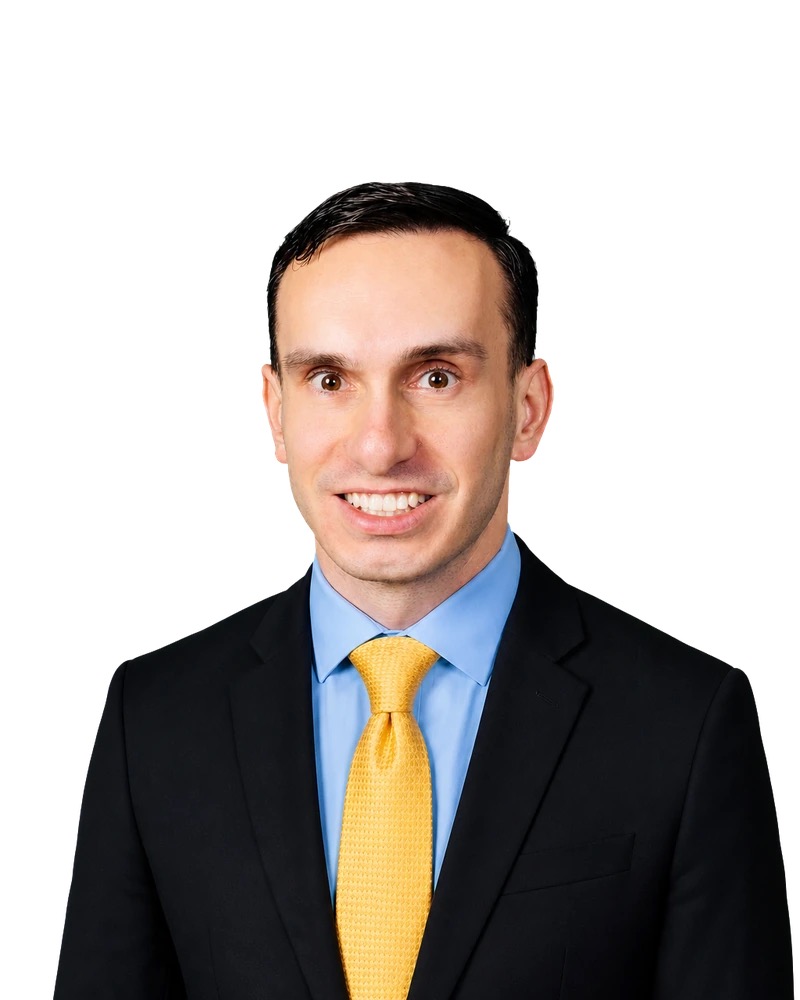 Professional portrait of Nico Hanley in a navy suit, blue shirt and gold tie.